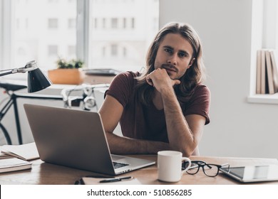 How may I help you? Confident young man with long hair holding hand on chin and looking at camera while sitting at his working place in office  - Shutterstock ID 510856285