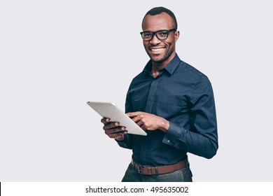 How may I help you? Handsome young African man holding digital tablet and looking at camera with smile while standing against grey background