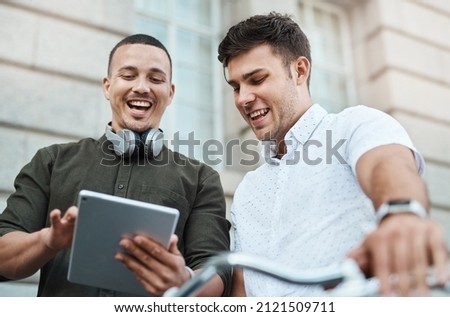 How millennials make things happen. Shot of two young businessmen using a digital tablet together while riding a bicycle in the city.