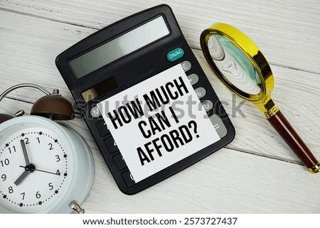 How much can I afford? text message on sticky note with magnifying glass, alarm clock and calculator on wooden background