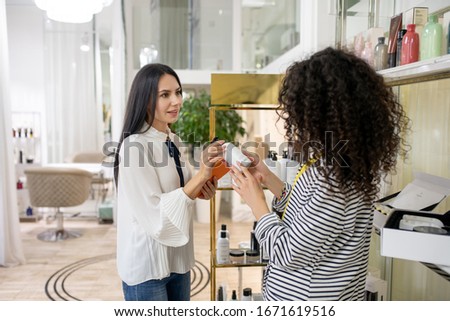 How much does it cost. Dark-haired woman in a striped jacket asking about price of body lotion