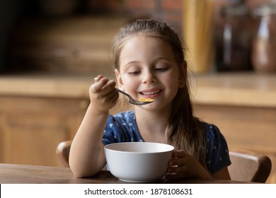 How tasty. Cute little girl enjoy eating cereal for morning breakfast with appetite. Hungry child holding full table spoon of sweet delicious corn oat flakes with milk honey feeling pleasure delight