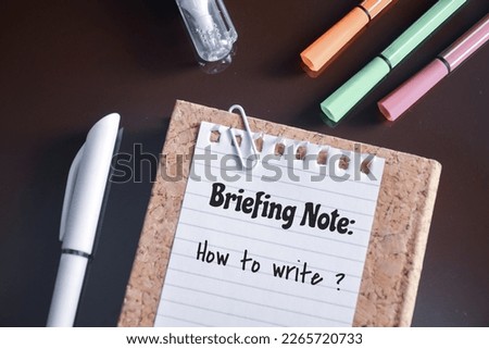 How to write a briefing note concept on torn piece of notepad paper on desk. Top view. 
