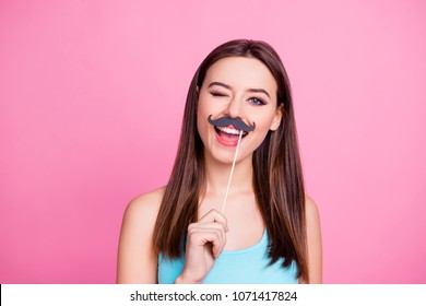 How are you doing? Portrait of charming joyful tender cheerful childish cute lovely cool woman with brown hairdress holding fake mustache on stick over mouth and winking, isolated on pink background
