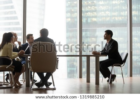 Hr team interviewing african male candidate sitting at big table in modern office, diverse recruiters talking to candidate making hiring decision for vacancy during job interview recruitment concept