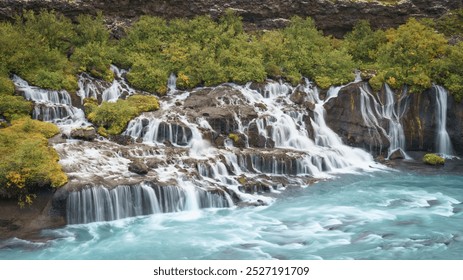 Hraunfossar waterfall cascading from lava rocks into the turquoise Hvítá River, surrounded by lush greenery. - Powered by Shutterstock