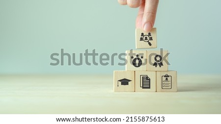 HRM and recruitment concept.  Job search, headhunting and recruitment process. Holding wooden cube with icons of education, qualification, cv, resume, skills and experience on smart grey background. 