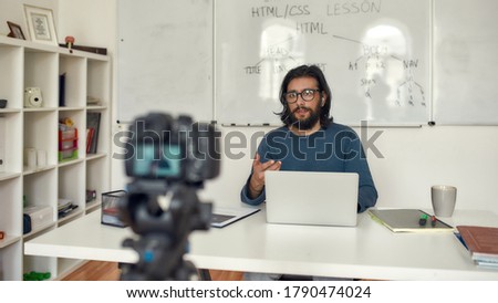 HTML online course. Professional male computer programming teacher giving online lesson, looking at camera while recording video tutorial. Focus on a man. E-learning. Distance education. Stay home
