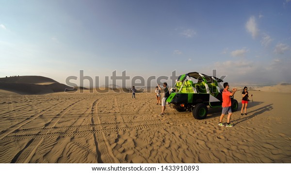 Huacachina, Peru - Apr 9, 2017: Buggy tour in the\
desert at sunset, people taking photos of sand dunes and\
sand-hills. Extreme sports, adventure, journey and travel concept.\
Wide angle shot.