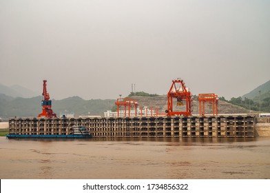 Huangqikou, Chongqing, China - May 8, 2010: Yangtze River. Landscape Of Rred Cranes On Multi-level Port Quay Behind Brown Water. Barge Docked, Green Foliage In Back Under Gray Smoggy Sky.