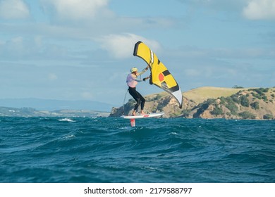 Huaraki Gulf, Auckland  New Zealand - 230221: A young man wing foils in the ocean between Great Barrier Island and Auckland, using a hand held inflatable wing and riding a hydrofoil surf board.