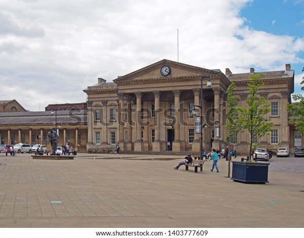 huddersfield, yest\
yorkshire, United Kingdom - 20 May 2019: people and taxis in saint\
georges square huddersfield in front of the facade of the historic\
victorian train\
station