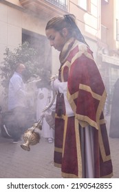 Huelva, Spain - April 10, 2022: Female Altar Boy Or Acolyte In The Holy Week Procession Shaking A Censer To Produce Smoke And Fragrance Of Incense