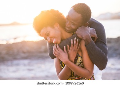 Hug And Enjoy Black African Race Couple Of Model Man And Woman Young 25 Yearso Old Stay In Love And Touch Joking And Playing Together. Sunset In The Background At The Beach With Waves And Ocean. 