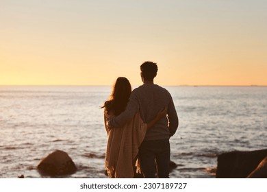 Hug, sunset and couple relax on beach in evening on holiday, summer vacation and weekend by ocean. Nature, love and man and woman embrace, hugging and calm for bonding, quality time and peace by sea - Powered by Shutterstock