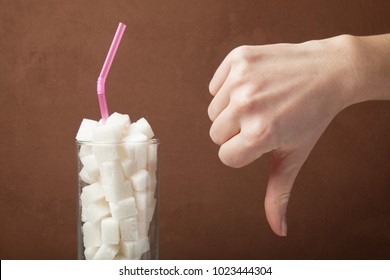 A Huge Amount Of Sugar In Juice Or Soda Drinks. Sugar Cubes In Glass And Hand Shows Thumbs Down.