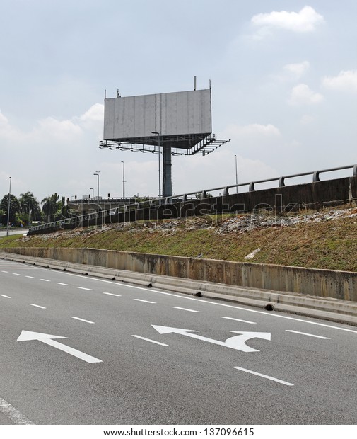 A huge blank unipole\
advertisement billboard along a motor highway with traffic arrow\
signage.