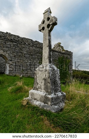 Huge Celtic cross gravestone standing in front of the ruins of Carran Church, The Burren National Park, County Clare, Ireland