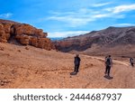 The huge Charyn Canyon in the desert of Kazakhstan. Several people descend to the bottom of the canyon for a walk on a hot day in jackets against the backdrop of mountains and snowy peaks