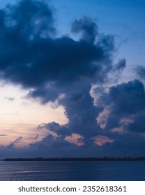 A huge cloud above harbor during blue hour. Residue of pink and red color from sunset behind cloud.
					Deep blue colored water, object on horizon