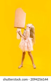 A huge delicious appetizing dessert. A girl holds a large ice cream on a stick in her hands, her head thrown back and looks at it, on a yellow background