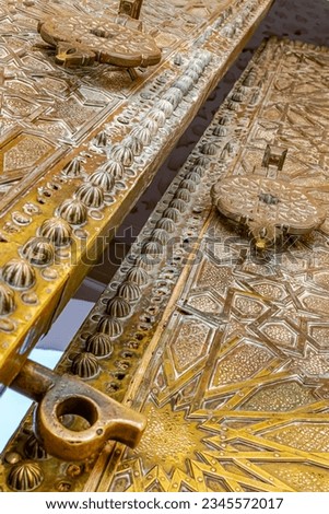 Huge door ajar with islamic andalusian 3D engravings and sculptures in Sidi Boumediene mosque of Tlemcen city in Algeria. A low angle view with metallic latch and handle and feature geometric patterns