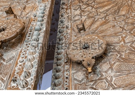 Huge door ajar with islamic andalusian 3D engravings and sculptures in Sidi Boumediene mosque of Tlemcen city in Algeria. A low angle view with metallic latch and handle and feature geometric patterns