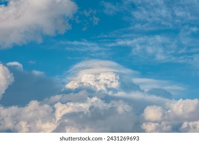 Huge dramatic lenticular cloud on white lush cloudy hill in blue sky. Beautiful cloudscape with big UFO shaped cloud in center. Scenic skyscape with altocumulus clouds. Awesome unusual cloudy skies.