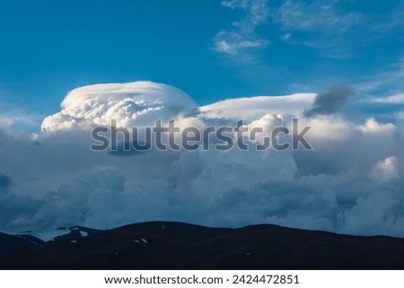Huge dramatic lenticular cloud on white lush cloudy hill in blue sky. Beautiful cloudscape with big UFO shaped cloud. Scenic skyscape with altocumulus clouds. Awesome fluffy unusual cloudy skies.