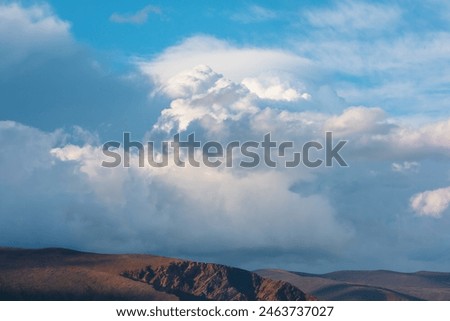 Huge dramatic lenticular cloud on white lush cloudy hill in blue sky. Beautiful cloudscape with big UFO shaped cloud in center. Scenic skyscape with altocumulus clouds. Awesome unusual cloudy skies.