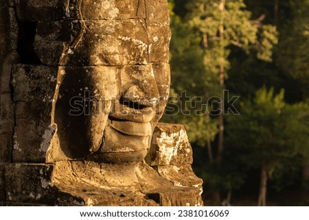 A huge face sculpted in stone, illuminated by the evening light at Bayon temple, Angkor, Cambodia.