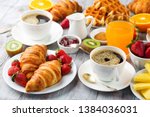 Huge healthy breakfast on white wooden table with coffee, orange juice, fruits, waffles and croissants. Selective focus. Good morning concept.
