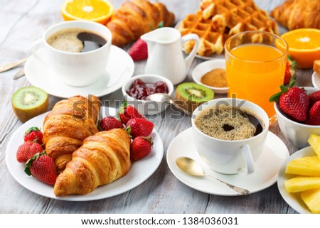 Huge healthy breakfast on white wooden table with coffee, orange juice, fruits, waffles and croissants. Selective focus. Good morning concept.