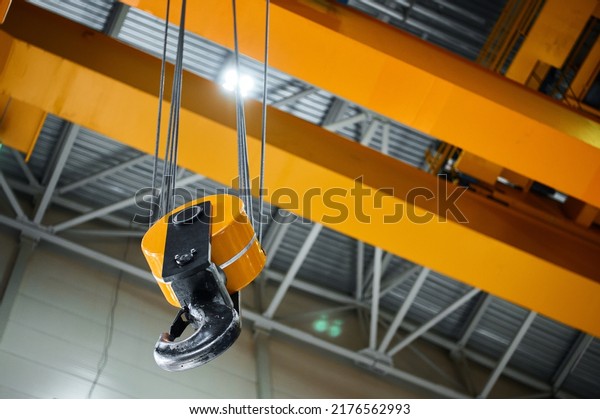 Huge\
hook assembly of bright yellow moving crane hangs under ceiling in\
workshop of production plant close low angle\
shot