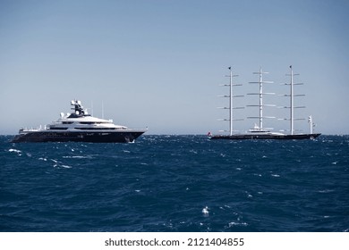 Huge motor megayacht and sailing yacht are near port of Monaco at sunset, water angle view, megayachts are moored in sea, sun reflection on glossy boards, big masts, clear weather