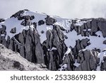 Huge mountain rocks covered in snow. The snow is slowly melting and you can see the water paths. It is cloudy day but the sun contures the shapes of the rocks. Mount Owen in New Zealand.