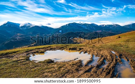 A huge muddy puddle with disgusting mud on a small path in the Carpathian mountains against the backdrop of beautiful autumn hills