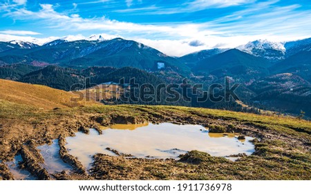 A huge muddy puddle with disgusting mud on a small path in the Carpathian mountains against the backdrop of beautiful autumn hills