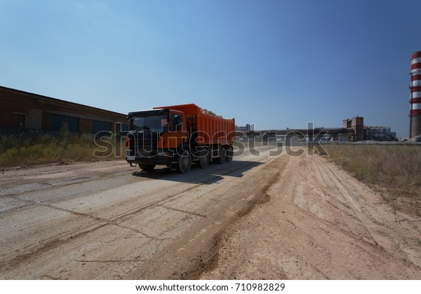 A huge\
orange tip truck with a shadow driving on a road on a natural\
background. Huge transporter in a sandy\
quarry.