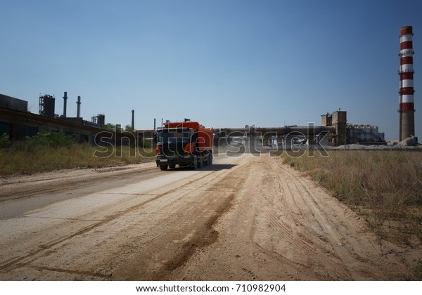 A huge\
orange tip truck with a shadow driving on a road on a natural\
background. Huge transporter in a sandy\
quarry.