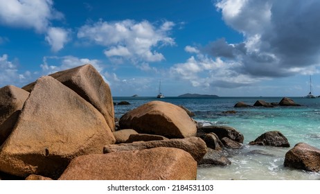 Huge picturesque boulders on the coast of the Indian Ocean are washed by turquoise water. Ships on the horizon. Clouds in the blue sky. Seychelles. Praslin Island.  Anse Lazio beach