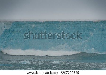 A huge piece of glacial ice wall has collapsed into sea causing a wave of ocean heading towards camera.Global warming .Climate Change