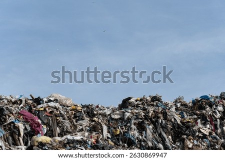 A huge pile of mixed garbage, refuse, and discarded materials is shown at a landfill. Birds fly overhead. 