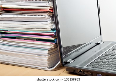 A Huge Pile Of Paperwork On A Desk Beside A Laptop Computer