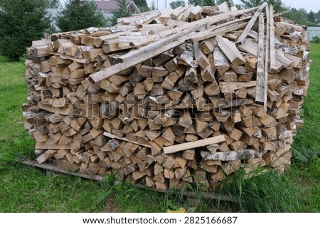 Huge pile of split logs and timber stacked outdoors on grass for winter heating