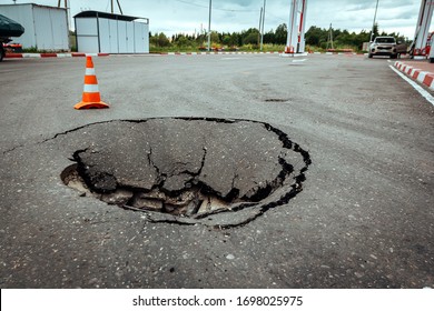 Huge Pit Sinkhole on Asphalt Road Surface and Traffic Cone restricting the movement of Cars. Accident situation on a City Street due to Cracks in Asphalt and Destruction or Collapse. Broken Hole