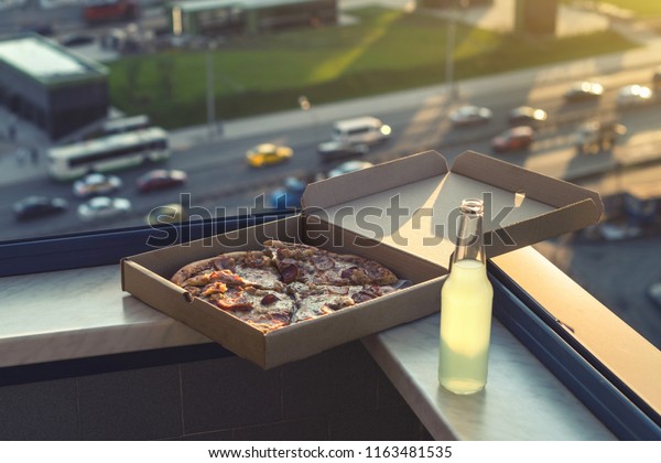 huge pizza in a box with a bottle of mojito on\
the sunset city background
