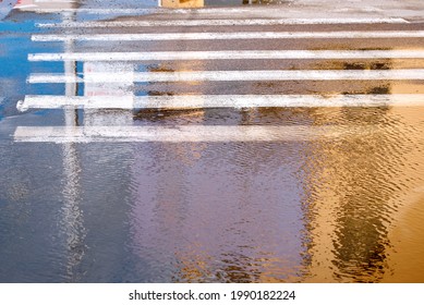 Huge puddles at sidewalk and pedestrian crossing. Pedestrian crossing after heavy rain. Puddles soaked zebra crossing in city street. Rainy background with puddles.