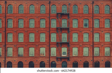 Huge red brick classic industrial building facade with multiple windows and fire escape ladder stairs. Industrial background. Loft inspiration. Construction facade concept. Vintage effect.