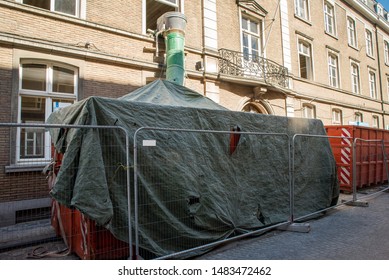 Huge Red Skip Covered In Green Tarpaulin Tarp To Stop Waste Rubbish Overflowing With A Slide For Workers To Throw Rubbish In The Skip Safely Red Hazard Construction Life Industrial Work 